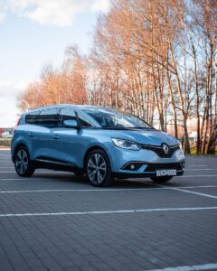 Une voiture Renault bleue brillante garée sur un terrain vide avec des arbres nus en arrière-plan.